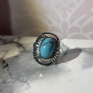 Silverring med turkos sten - Unik silverring med en stor, oval turkos sten i mitten. Ringen har en detaljerad design runt stenen och är även justerbar. Perfekt för att få lite mer färg till din outfit!