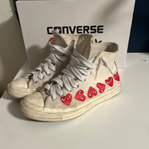 Converse x Comme des Garçons Play sneakers - Säljer ett par vita Converse x Comme des Garçons Play sneakers med de ikoniska röda hjärtana på sidan. Skorna har klassisk snörning och är i en hög modell. De är mycket anvönda 