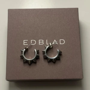 Silvriga örhängen med nitar från Edblad - Snygga silvriga örhängen från Edblad med coola nitar runt om. Perfekta för att ge en edgy touch till din stil. Kommer i originalförpackning.