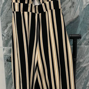 Randig byxdress från new yorker  - Snygg randig byxdress från new yorker i svart, beige och vit. Byxdressen har breda axelband och en liten utskärning framtill. 