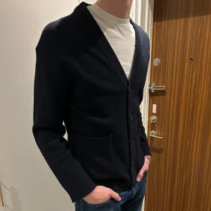 Mörkblå kofta från Lindbergh - Snygg mörkblå kofta från Lindbergh i lammull. Den har en bekväm passform med knappar framtill och två fickor. Perfekt att använda för lager på lager med t-shirt elr skjorta.                           Använd en enstaka gång och är i helt ny skick.               Nypris -:799