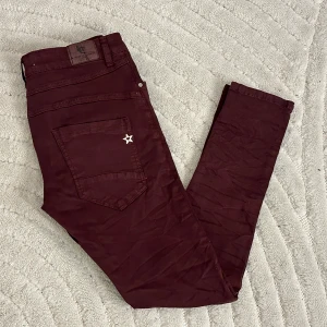 Coola byxor med stjärndetalj ❤️ - Snygga byxor med en cool stjärndetalj på bakfickan. Byxorna har knappar framtill och dragkedjor vid fickorna. Riktigt coola ❤️Färg: vinröda / bordeaux. Använda men fint skick! Hela och rena