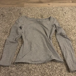 Grå långärmad topp - Säljer en stilren grå långärmad topp i mjukt material. Perfekt för en avslappnad look eller som basplagg i garderoben. Passar till många olika outfits!