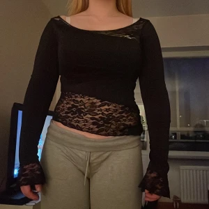 Svart spetsdetaljerad topp - Snygg svart topp med spetsdetaljer och långärmad design. Perfekt för en stilfull look med en touch av elegans. Toppen har en åtsittande passform och är idealisk för att lyfta din outfit.