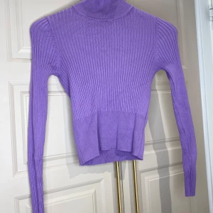 Lila ribbad polotröja - Snygg lila polotröja med ribbad design. Tröjan har en croppad passform och långa ärmar, perfekt för en trendig look. Den höga kragen ger extra värme och stil.