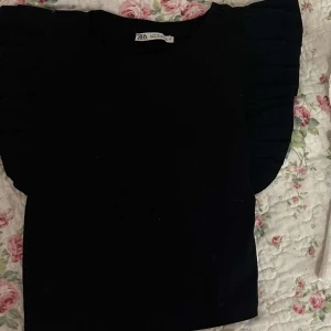 Svart kortärmad tröja - Svart kortärmad tröja med volanger på axlarna, sitter väldigt bra. 