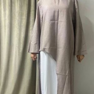 Abaya/Klänning - Elegant beige abaya i one size med asymmetrisk design som ger en unik och stilren look. Vida ärmar och luftigt material gör den både bekväm och perfekt för alla tillfällen – vardag som fest. Den har aldrig använts, endast provad för bilder. Enkel att styla med valfritt underlager (den vita klänningen på bilden ingår inte).   Hör av dig vid intresse!