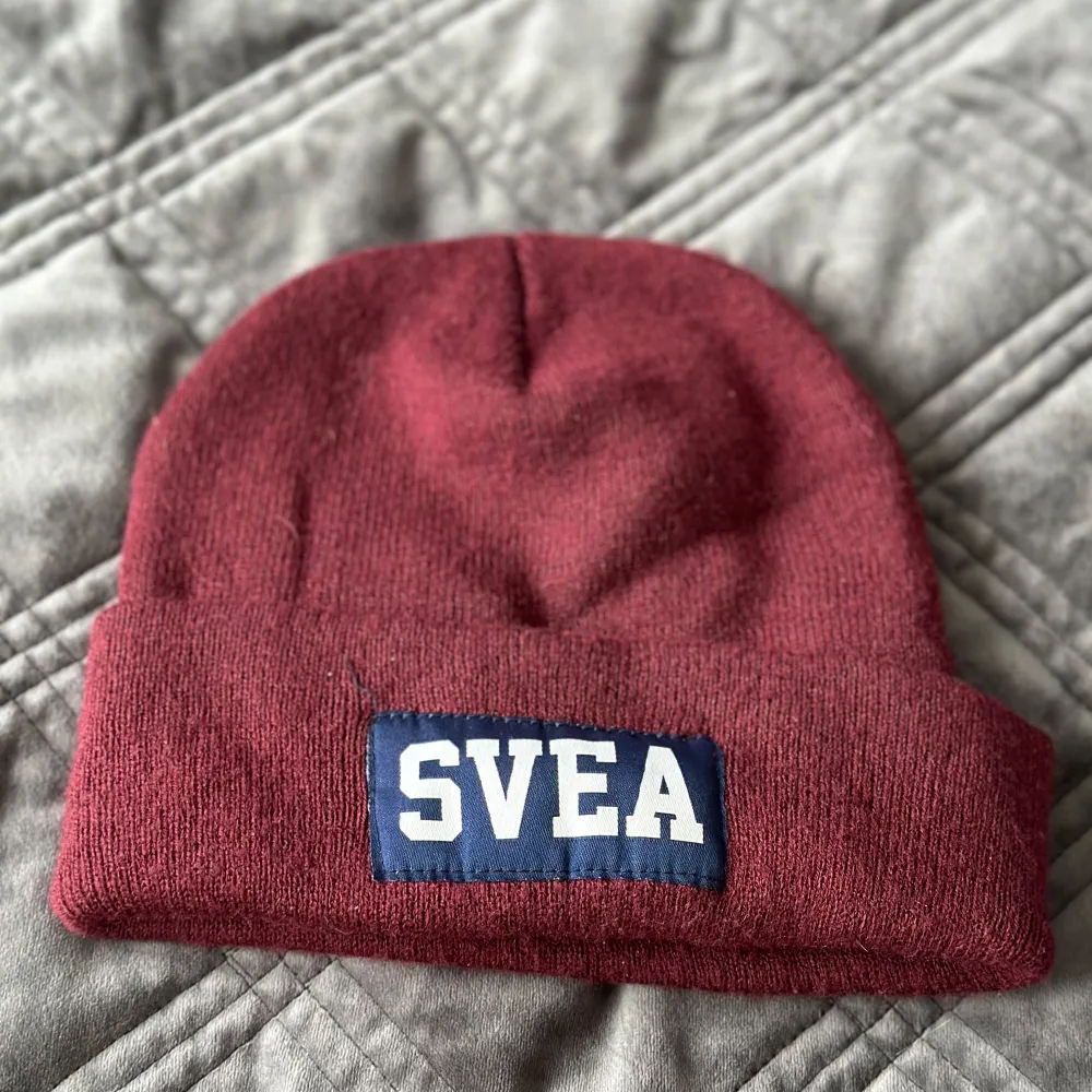 Säljer en snygg vinröd mössa från Svea i bra skick. Den har en uppvikt kant med Svea-loggan i vitt på en blå bakgrund. Perfekt för att hålla sig varm under höst och vinter!. Accessoarer.