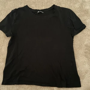 Svart t-shirt från Zara - Säljer en klassisk svart t-shirt från Zara i storlek S. Den är kortärmad och perfekt för vardagsbruk. Materialet känns mjukt och bekvämt, vilket gör den till ett bra val för både avslappnade och mer uppklädda tillfällen💕