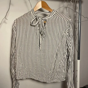 Randig blus med knytband  - Storlek M enligt lapp men liten i storleken. En knapp saknas, se bild.