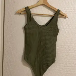 Säljer en snygg olivgrön bodysuit med ribbad struktur. Den är ärmlös och har en tight passform, perfekt för både vardag och fest. Materialet är mjukt och stretchigt, vilket gör den superbekväm att bära.