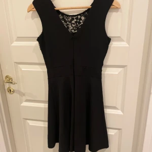 Svart klänning med spetsdetaljer - Säljer en elegant svart klänning i storlek S. Den har en vacker spetsdetalj på överdelen och är ärmlös, vilket gör den perfekt för festliga tillfällen. Klänningen har en normal passform och en dragkedja i ryggen för enkel påklädning. Den är i nyskick och redo för nästa ägare!