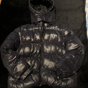 Svart dunjacka från night addict - Säljer en svart dunjacka från night addict. Jackan har en avtagbar huva och dragkedja framtill. Perfekt för kalla dagar med sin quiltade design och långa ärmar. Den är använd ett fåtal gånger och skicket är som nytt, bvsa