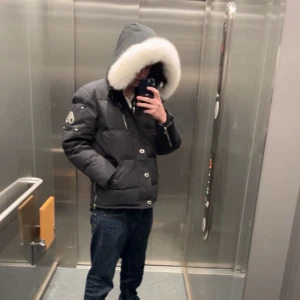 Svart dunjacka från Moose Knuckles - Säljer en svart dunjacka från Moose Knuckles med en stor, fluffig vit pälskant på huvan. Jackan har broderad logga på ärmen och fram, samt knappar och dragkedja framtill. Perfekt för kalla vinterdagar. Om ni e intresserad hör av er!!! Jackan är i storlek L men passar som M!! Säljer denna pågrund av att jag köpt ny jacka