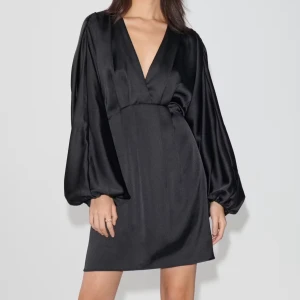 Ginas populära satin mini dress  - Elegant svart klänning med djup v-ringning och långa, vida ärmar. Tillverkad i ett glansigt material som ger en lyxig känsla. Perfekt för en stilren och sofistikerad look. Helt ny med lapp kvar! 