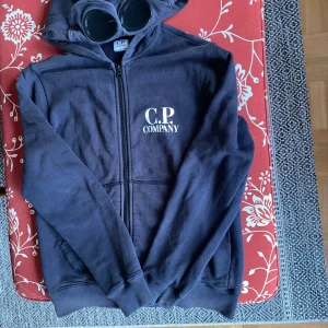 Mörkblå hoodie från C.P. Company - Säljer en mörkblå hoodie från C.P. Company. Sköna glasögon, passar perfekt med keps eller mössa. Storlek 160cm men passar mig som är 168cm. Kan bevisa att den är autentisk. Köpt för 2200. Kan gå ned i pris vid enkel och snabb affär. Står inte för fraktens slarv