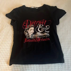 Svart t-shirt med Detroit-tryck - Snygg svart t-shirt med ett coolt tryck av en kvinna och texten 'Detroit & Detroit Friends' i rött och vitt. Är i barn storlek, jag har vanligtvis på mig S eller M på toppar men den passar bra ändå! Lite tajt om man har större bröst (det är därför jag behöver sälja den 🥹😔) skriv om ni vill ha bilder på något speciellt 💗🫶