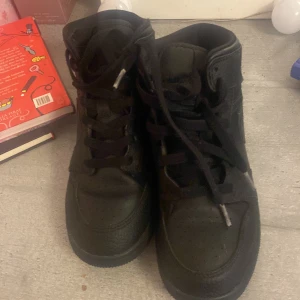 Svarta Nike sneakers - Säljer ett par svarta Nike sneakers med hög snörning och klassisk design. Skorna har en stilren look med diskreta detaljer och är perfekta för en casual stil.