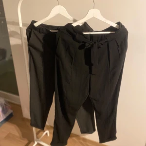 Svarta byxor från Gina Tricot - Snygga svarta byxor från Gina Tricot med knytband i midjan. Byxorna har en elegant design och är perfekta för en stilren look. De är högmidjade och har en rak passform som ger en bekväm känsla.