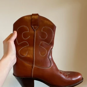 Bruna cowboy boots i skinn - Snygga vintage bruna cowboy boots i skinn med dekorativa sömmar. Tycker väldigt mycket om dem men tyvärr är de för stora för mig 