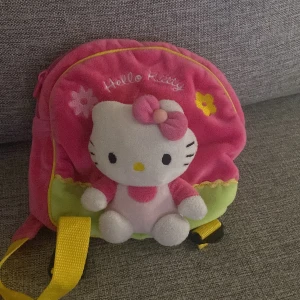 Rosa Hello Kitty ryggsäck - Söt rosa ryggsäck med Hello Kitty-motiv och blommor. Väskan har gula axelband och en dragkedja för enkel öppning. Perfekt för folk som älskar Hello Kitty!💕