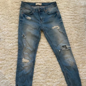 Blå jeans från Gina Tricot - Snygga blå jeans från Gina Tricot med slitna detaljer för en trendig look. Modellen är tight och passar perfekt för en casual stil. De har snygga dragkedjor nertill som en snygg detalj. Jeansen är i strl 29/30 och passar ungefär S. Innerbenslängd=67cm❤️  OBS! Köpare står för frakten!