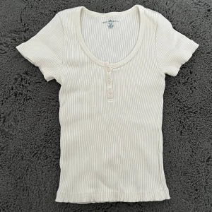 Brandy Melville topp - Säljer en krämvit ribbad topp från Brandy Melville med korta ärmar och knappar framtilll. Toppen är i ett mjukt och stretchig bomullmaterial💗