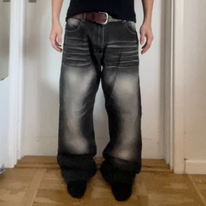 Svarta baggy jeans med bruna detaljer - Säljer ett par svarta baggy jeans med coola slitningar och en unik brun bakficka. Perfekta för en avslappnad stil med en touch av edge.