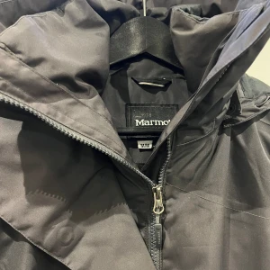 Marmot jacka i vattenavvisande tyg. Grå-lila i fint skick! - Längre modell av jacka i vattenavvisande material, något fodrad. Mycket fint skick. Kommer från ett rök- och djur fritt hem. Färgen är något grå-lila, bilderna inte helt rättvisande.