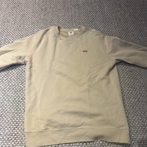 Beige sweatshirt från Levi's - Säljer en stilren beige sweatshirt från Levi's med rund hals och liten röd logga på bröstet. Tröjan har långa ärmar och ribbade muddar vid ärmslut och nederkant. Perfekt för en avslappnad look. Inga fläckar eller skador. Kontakta mig vid minsta fundering🙏🏻🙌