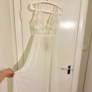 Långklänning med spets/pärldetaljer - Elegant vit långklänning med v-ringad spetsöverdel med skimrande pärlor och tunna axelband. Kjolen är flödande och ger en romantisk känsla. Perfekt för speciella tillfällen.