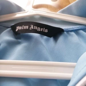 Blå track jacket från Palm Angels - Snygg ljusblå track jacket från Palm Angels med vita och svarta ränder längs ärmarna. Jackan har dragkedja framtill och två fickor. Perfekt för en sportig look. Pris går att diskutera 