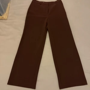 Bruna kostymbyxor - Snygga bruna kostymbyxor med en klassisk design. Byxorna har en rak passform och är perfekta för en stilren look. Tillverkade i ett bekvämt material som passar bra för både vardag och mer formella tillfällen.