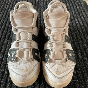 Nike Air sneakers i beige och svart - Snygga Nike sneakers i beige med svarta detaljer. Skorna har en unik design med stora bokstäver på sidorna och en bekväm passform. Perfekta för en sportig look.