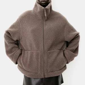 Brun teddyjacka med dragkedja - Mysig brun teddyjacka med hög krage och dragkedja framtill. Jackan har två praktiska fickor och en avslappnad passform.