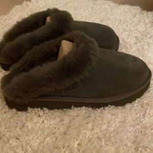 Grå tofflor från UGG (äkta) - Mysiga grå tofflor från UGG med mjuk pälsfodring. Perfekta för att hålla fötterna varma under kalla dagar. Aldrig använda då jag fick dem nu på jul oxh har redan ett par. Storlek 39 men passar både 38 och 40. Modellen heter Cluggette och nypris ligger på 1 700. Skorna går att använda inne som ute då dem har en lite tjockare sula.