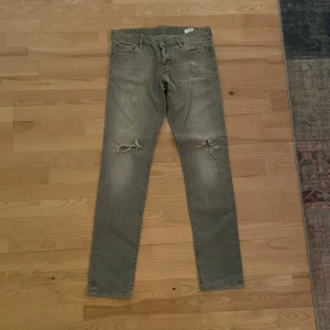 Grå jeans från Dsquared2 - Säljer ett par grå jeans från Dsquared2 med slitna detaljer på framsidan. Perfekta för en avslappnad stil. Nypris ca 4000. Hör gärna av er om ni har några frågor.