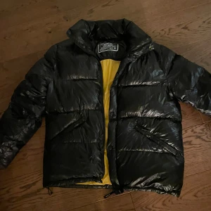 Svart pufferjacka Replay - Säljer en snygg svart pufferjacka från Replay med gul insida. (Insidan syns inte när man har på sig den) Jackan har en hög krage och dragkedja framtill. Den är i XL men sitter definitivt som en L i formen. Perfekt för kyliga dagar. Den är bra skick förutom att fodringen klämts ihop lite vid armhåla som puffer jackor brukar göra. Priset kan diskuteras :) 