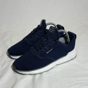 Mörkblå sneakers från Gant - Snygga mörkblå sneakers från Gant med vit sula och snörning. Skorna har en stickad ovandel som ger en modern look och bra andningsförmåga. Perfekta för en avslappnad stil. Storleken är 41