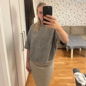 Grå stickad T-shirt från & other stories - Säljer en stilren grå tröja med trekvartsärm. Tröjan har en lös passform som ger en bekväm känsla.