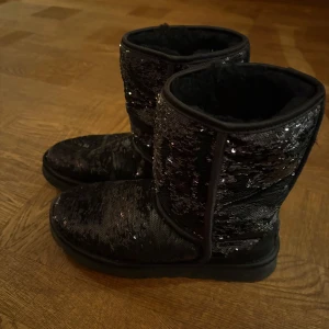 UGG - Snygga svarta boots med glittriga paljetter som ger en extra touch. Perfekta för att lysa upp vinterdagarna. De har en bekväm och varm insida, idealiska för kyligare väder.