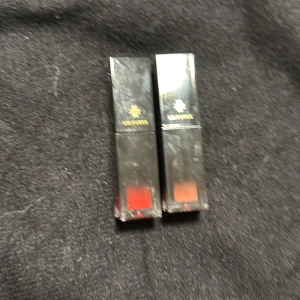 Två läppstift från Lip Power - Säljer två eleganta läppstift från Lip Power. Förpackningarna är svarta med en genomskinlig botten som visar färgerna, en i röd och en i orange nyans. Perfekta för att ge en färgstark touch till din look.