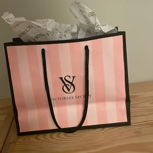 Rosa shoppingväska från Victoria's Secret - Säljer en superfin rosa shoppingväska från Victoria's Secret. Den har ett klassiskt randigt mönster i olika nyanser av rosa och svarta handtag. Perfekt för shoppingrundan eller som presentpåse. Väskan är i nyskick och kommer med originaltissuepapper. Passa på att köpa denna ikoniska väska!😜😜😎💘