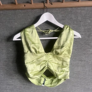 Ljusgrön satin topp - Säljer en superfin ljusgrön satin topp med knytband i nacken. Toppen har en snygg rynkad detalj framtill och är perfekt för sommaren. Den är axelbandslös och har en glansig finish som ger en lyxig känsla. Perfekt för en festlig kväll eller en dag på stan! Bara använd en gång. Pris går att diskutera.