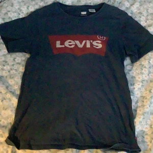 Svart t-shirt från Levi's - Säljer en svart t-shirt från Levi's i storlek XXS. Den har en klassisk rund hals Levi's-loggan i rött och vitt på framsidan. Perfekt för en casual look eller att matcha med jeans. T-shirten är i bomull och känns skön mot huden.