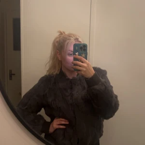 Grå pälsjacka från Hollies - Säljer en supermjuk och stilren grå pälsjacka från Hollies. Den har långa ärmar och ribbade muddar som håller kylan ute. Perfekt för höst och vinter när du vill vara både varm och snygg. Jackan är i bra skick och passar perfekt till både vardag och fest. Den är lite sliten vid handleden men det är inget man tänker på. 