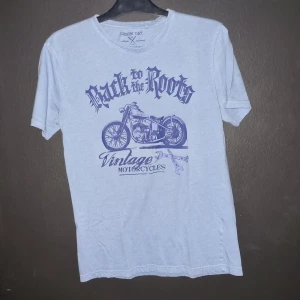 Blå t-shirt med motorcykeltryck från Denim Day - Säljer en blå t-shirt från Denim Day i storlek medium. Den har ett coolt blått tryck med texten 'Back to the Roots' och en vintage motorcykel.