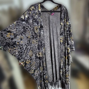 Mönstrad kimono från Indiska - Superfin kimono från Indiska i storlek L/XL. Den har ett vackert blommigt mönster i svart, grått och guld med fransar nedtill. Materialet är luftigt och är som sammet på utsidan. 