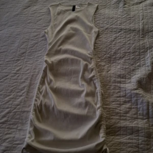 Vit ribbad klänning från H&M Divided - Säljer en stilren vit ribbad klänning från H&M Divided i storlek XS. Klänningen är ärmlös och har en tight passform med snygga rynkdetaljer längs sidorna. Perfekt för en chic och enkel look. 🌟 superbra skolavslutningsklänning eller för student.  Möts bara upp