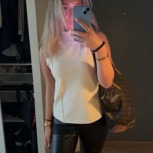 Beige ärmlös polotopp - Snygg beige ärmlös polotopp med hög krage. Perfekt för en stilren look och kan matchas med både jeans och kjol. Enkel och elegant design som passar till många tillfällen.